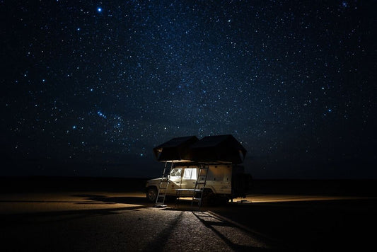 A LandCruiser with a rooftop tent in a South African desert in front of a starry sky.
