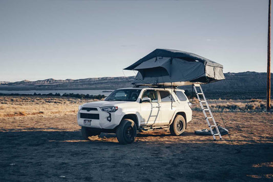 A rooftop tent sits assembled on top of an SUV, which itself sits on an open plain.